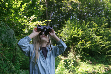 Fototapeta premium Cute little girl exploring nature looking through binoculars. Child playing outdoors. Kids travel, adventure and bird watching concept.