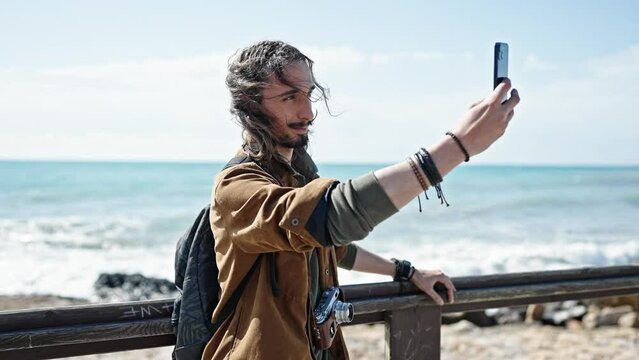 Young hispanic man tourist wearing backpack make selfie by smartphone at seaside