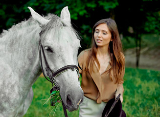 Obraz premium Young girl standing with a grey horse on a grass. Learn horseback riding through lessons. Explore horse therapy, hippotherapy. A woman and her grey horse in a forest, bonding with animals.
