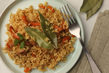 Delicious pilaf, bay leaves and fork on white table, flat lay