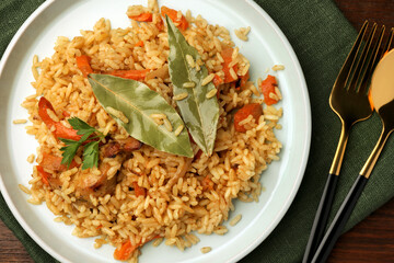 Delicious pilaf and bay leaves served on table, flat lay