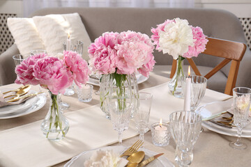 Stylish table setting with beautiful peonies and burning candle indoors