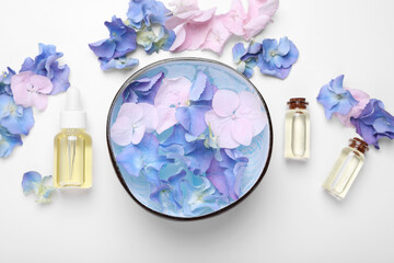 Spa composition. Aromatic water in bowl, flowers and bottles of essential oil on white background, flat lay