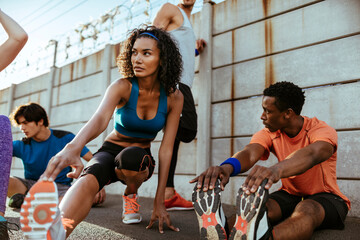 Young and diverse group of people stretching before going on a jog and running together in the city