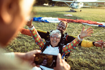 Senior man taking a picture of his wife after landing from a skydive with her instructor