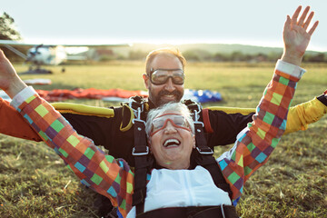 Senior woman skydiving with her instructor and landing on a field with their parachutes