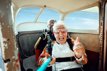 Scared senior woman getting ready to skydive out of an airplane with her skydiving instructor