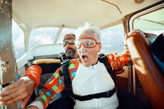 Scared senior woman getting ready to skydive out of an airplane with her skydiving instructor