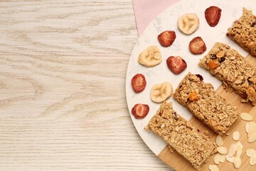 Obraz na płótnie Canvas Tasty granola bars, dried strawberries, bananas and almond flakes on wooden table, top view. Space for text