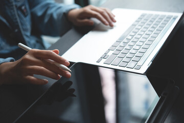 Closeup of business woman hand with stylus pen using digital tablet and working on laptop computer,...