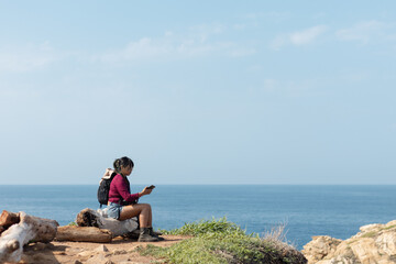 Fototapeta na wymiar Young tourist sitting on a log checking her phone and texting in the morning near the camping area on the beach of Mazunte Oaxaca
