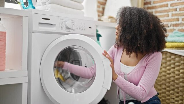 African american woman washing clothes holding dirty shirt looking upset at laundry room