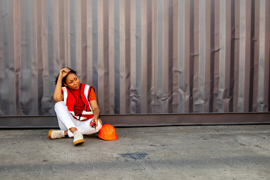 Young African American female worker leaning on container alone with  headache tired serious stress and worry from overwork and exhaustion, holding her head unthinkable from overworked trouble.