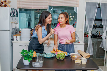 Best friends relationship and caring daily life of two asian young women living together : Delicious dinner with vegetable salad healthy food eating tasty tomatoes on kitchen table in townhome.