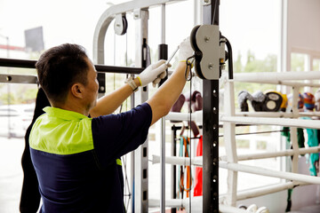 Professional Asian male service worker or fitter checks equipment, maintains and secures fitness...
