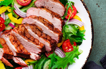 Salad with grilled duck breast slices and cherry tomatoes, cucumber, paprika, red onion, lettuce and arugula on green table background, top view