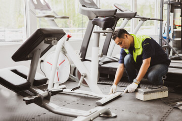 Professional asian male service repair worker or sport fitter using bicycle and treadmill service equipment, supervising and securing fitness equipment in indoor gym.