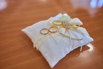 Wedding rings on white pillow with lace and beads. Unusual engagement rings on decorative hand made...