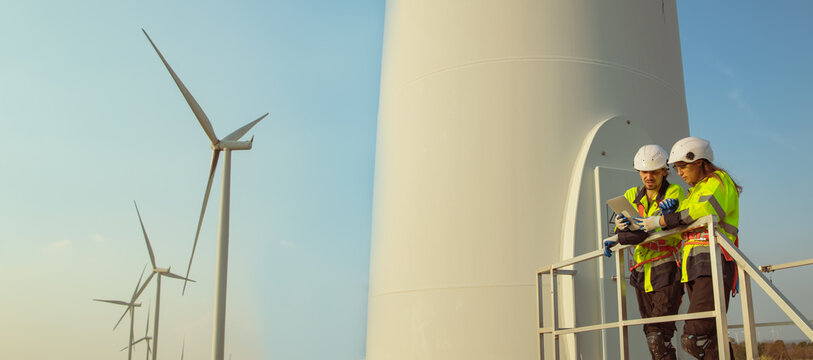 Technician working outdoors, wind farm professional team male and female safety uniform ready to perform maintenance duties for the wind turbine tower in the summer clean energy wind turbine farm.