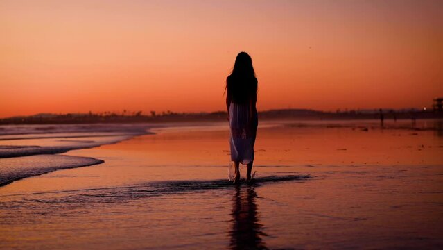 Pretty Asian woman enjoys a walk on the beach at sunset.