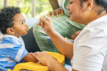 Caring father and mother take care health care of his African-Thai son feeding him delicious and nutritious lunch : Portrait baby boy who enjoys eating food relishing and gluttonous.