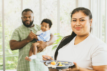 Portrait happy family couple, African American father and Asian mother in a good mood. Healthy lifestyle with cute half-Thai-Nigerian son and mother holding tray of food for her son to have lunch.