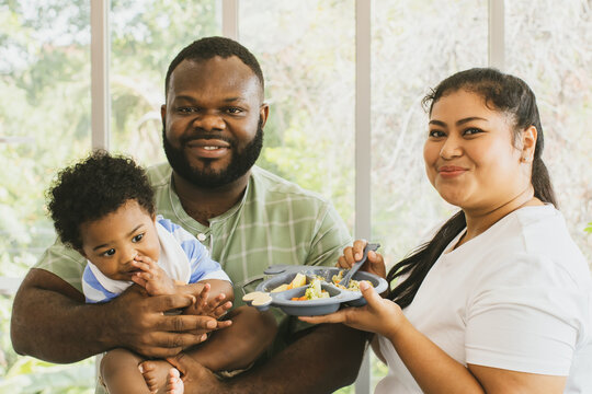 Portrait Happy Family Couple, African American Father And Asian Mother In A Good Mood. Healthy Lifestyle With Cute Half-Thai-Nigerian Son And Mother Holding Tray Of Food For Her Son To Have Lunch.