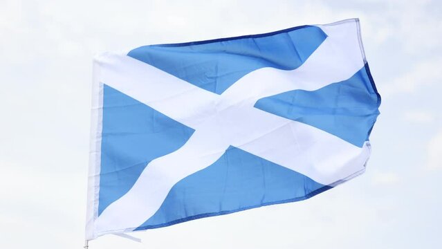 Against backdrop of blue sky, national flag of country Scotland flutters on flagpole. 