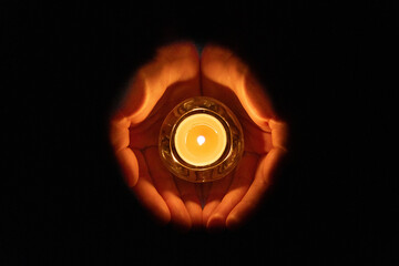 Human palm hands holding burning candle in dark black background. 