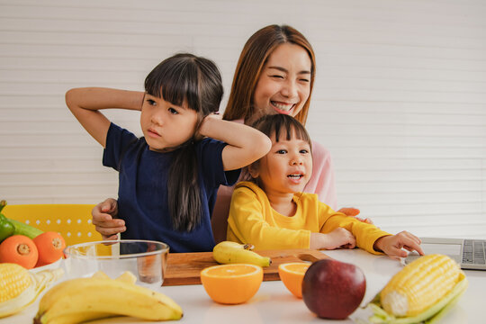 Happy mother teaches two young daughters how eat fruits vegetables healthy nutrition while listening but the eldest daughter is deaf and disinterested covering her ears with frowning and touchy hands.