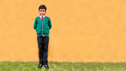 Fototapeta na wymiar Dark-haired 9-year-old Latino boy in a public school uniform is excited and happy about the return to school ready to study