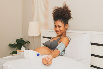 African American pregnant woman health care herself at home measuring her own blood pressure with...