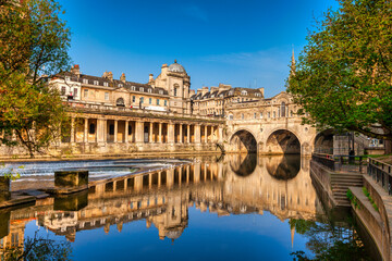 Pulteney Bridge and Weir on the River Avon in the historic city of Bath in Somerset, England, on a bright spring morning with deep blue sky. Stunning reflection, which is genuine.  