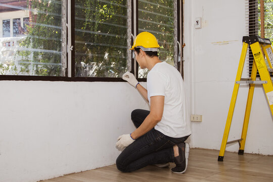 Male staff, Asian termite exterminators wearing hard hats inspecting old wooden window sills to detect termite nests, insects and areas where termites cause housing problems to eliminate and prevent.