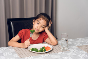 Little cute kid girl refusing to eat healthy vegetables. Children do not like to eat vegetables.