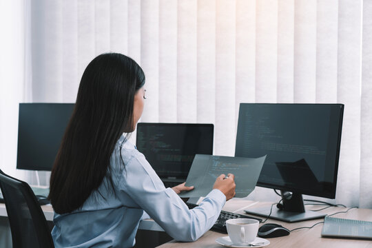 Asian woman software developers sitting in front of computers looking at computer codes on the screen.