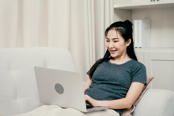 Asian woman sits back on the sofa using a laptop computer to work at home.