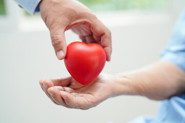 Asian man doctor give red heart to elderly woman patient for good health in hospital.
