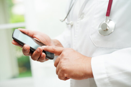 Asian Woman Doctor Holding Mobile Phone Or Tablet For Search Method Of Treatment Patient In Hospital.