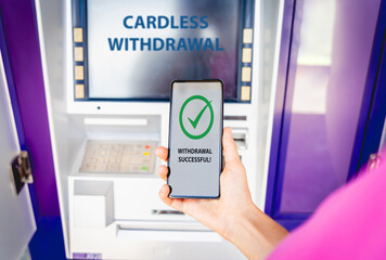 Young woman using the smart phone for cardless withdrawing the cash near the ATM