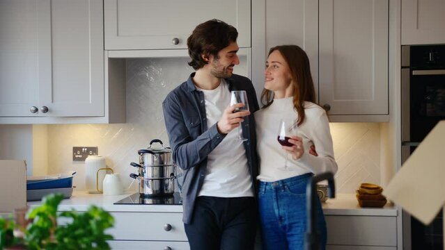 Excited couple celebrating with glass of red wine in kitchen of new home as they unpack boxes on moving in day together - shot in slow motion