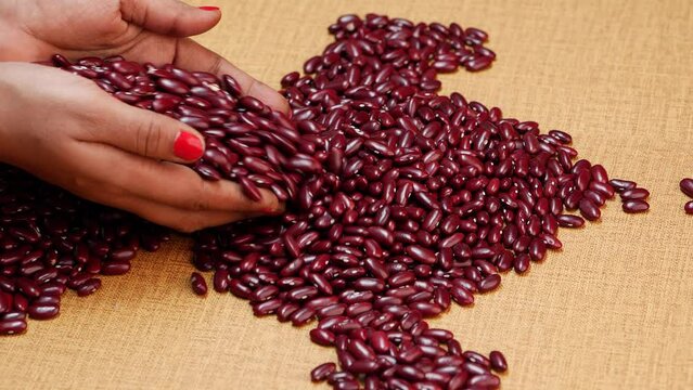 On A Table, Red Beans Are Seen - A Woman's Hands Picking Up One Pile While Another Hand Holds Another