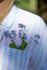 Decoration of bouquet of delicate forget-me-nots looks great in pocket of blue striped cotton shirt of unrecognizable . 