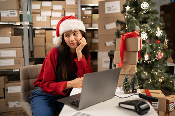 Young woman wearing Santa hat working in a warehouse. Thoughtful Online store owner making plans...
