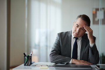 Stressed mature businessman sitting at desk thinking about upcoming meeting