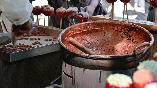 Candied    / roasted  almonds are cooked by hot brown sugar  in a pan and  dipped in the sugar mixture at open air fair.