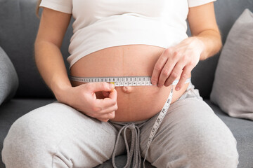 pregnant girl sitting and measuring her belly with a measuring tape
