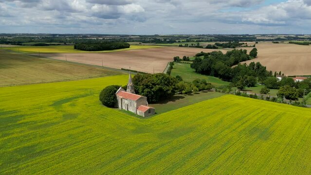 Aerial view French Countryside, Yellow rapeseed field panorama with wind turbine or wind wheels, Sainte-Radegonde Chapel, Courant, Charente Maritime, France, High quality 4k footage