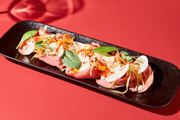 Closeup of an Asian appetizer; meat, veggies, mushrooms on a black plate against a dramatic dark red velvet backdrop.