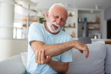 Senior man with arm pain.Old male massaging painful hand indoors. Old man hand holding his elbow...